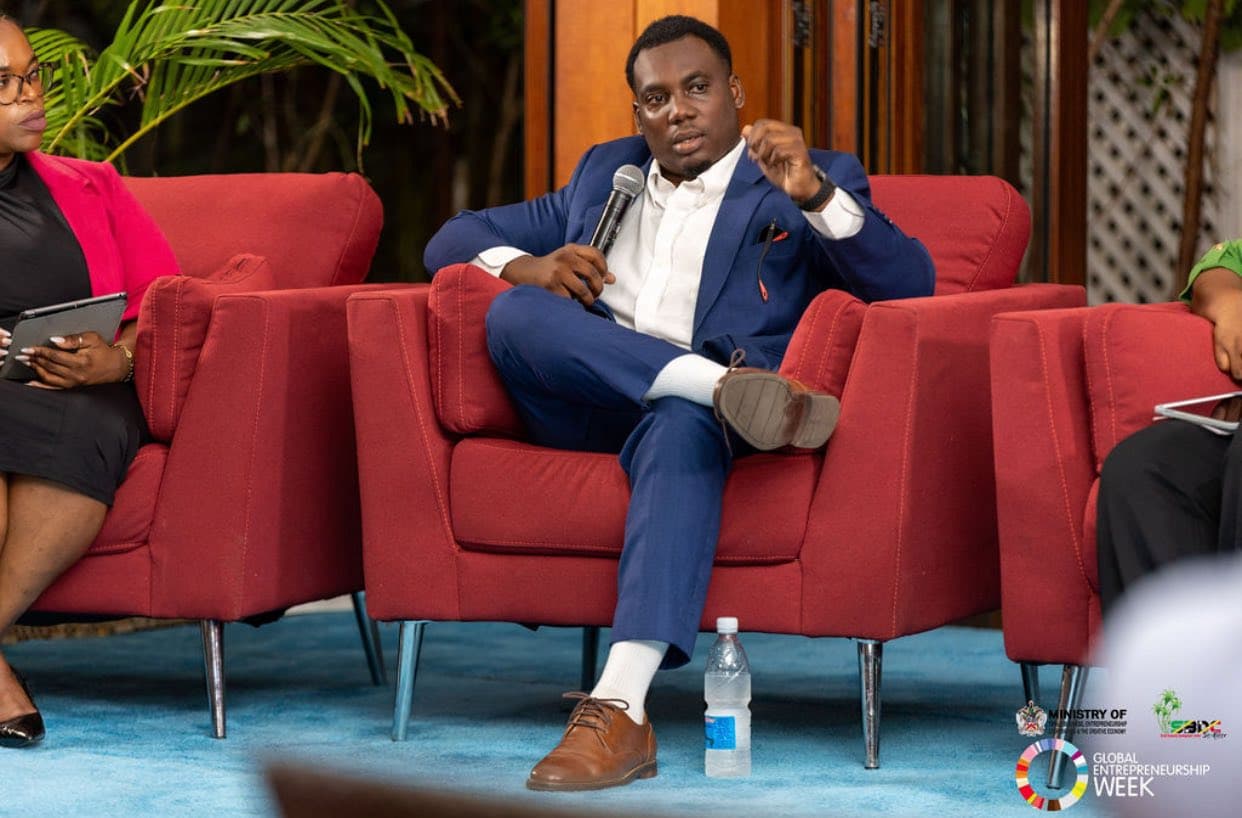 Man in a blue suit speaking into a microphone while sitting in a red armchair.